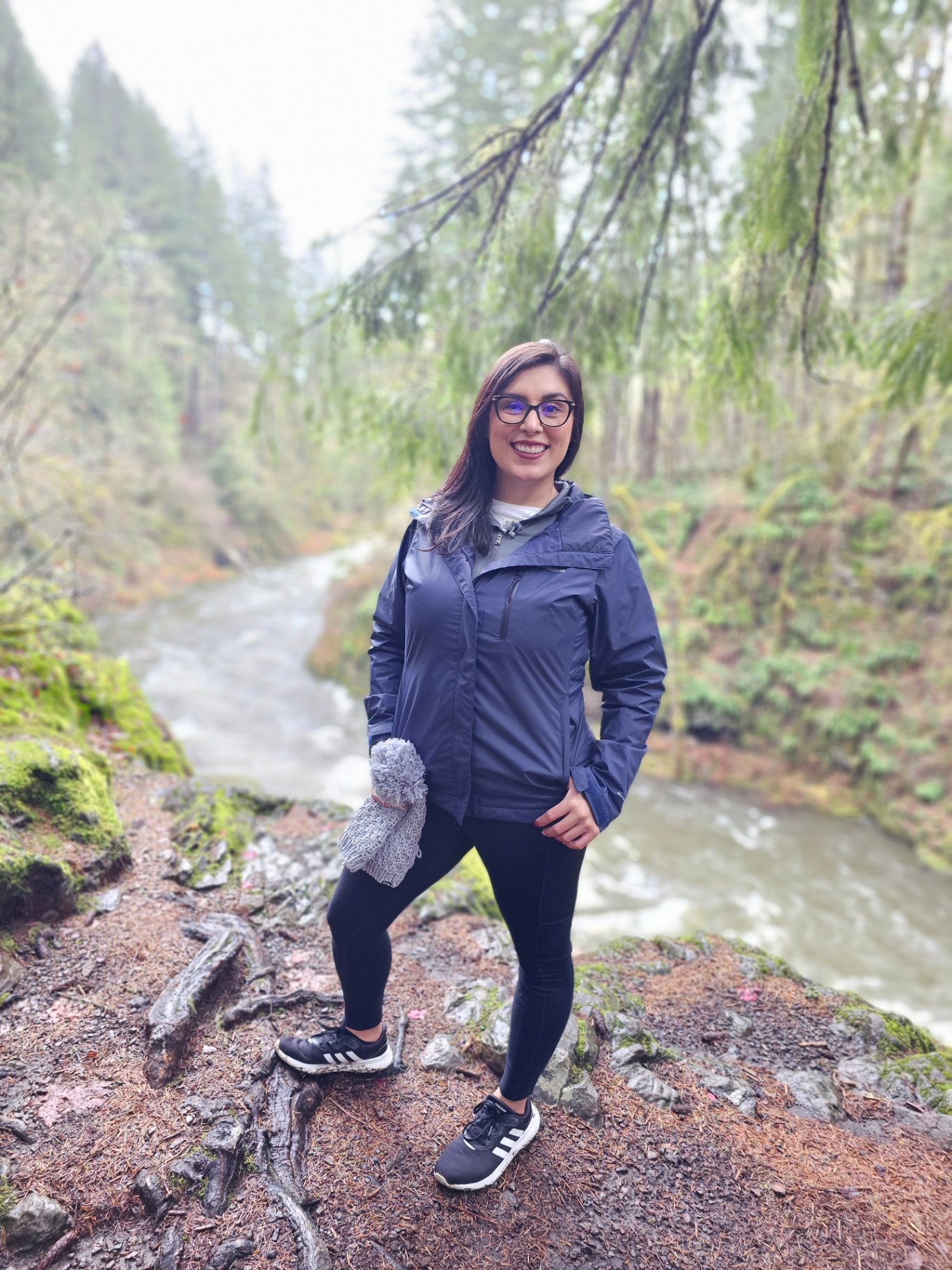 Woman standing beside a rushing creek in a mossy evergreen forest