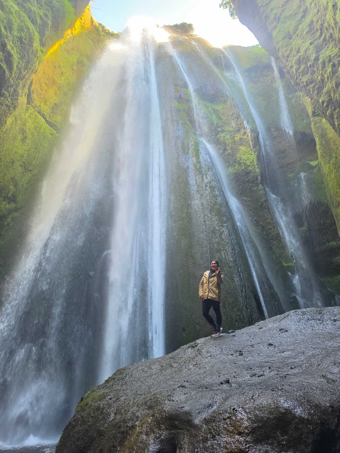 Woman standing on a rock beneath a towering Icelandic waterfall