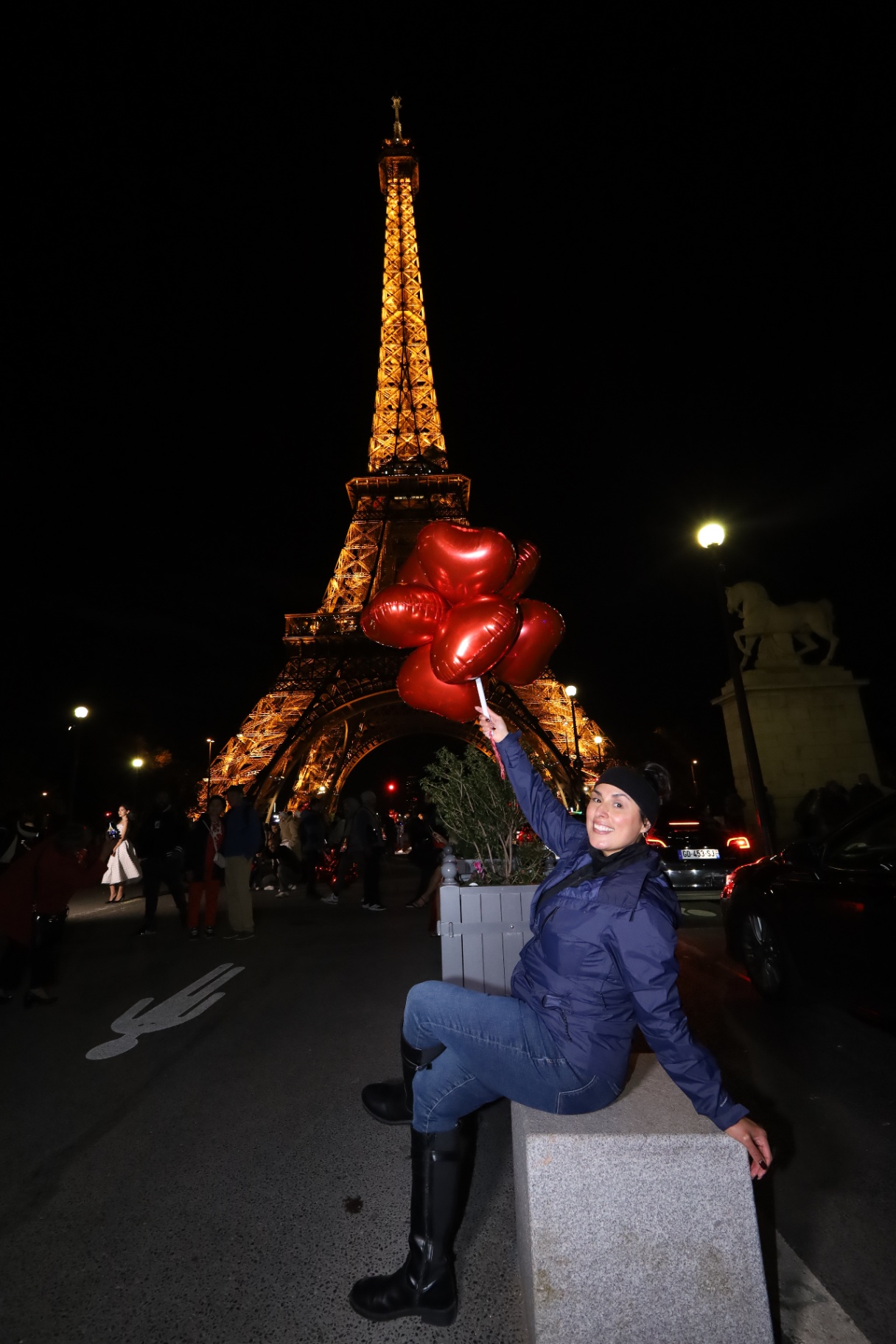 Woman holding red heart balloons in front of the Eiffel Tower at night