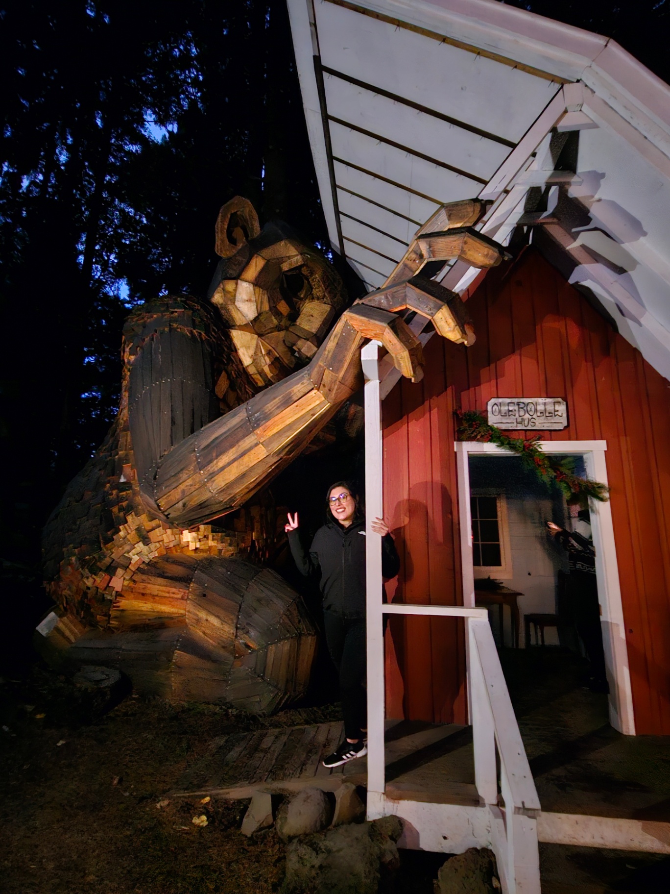 Woman posing beside a giant wooden troll sculpture beside a red cabin at night