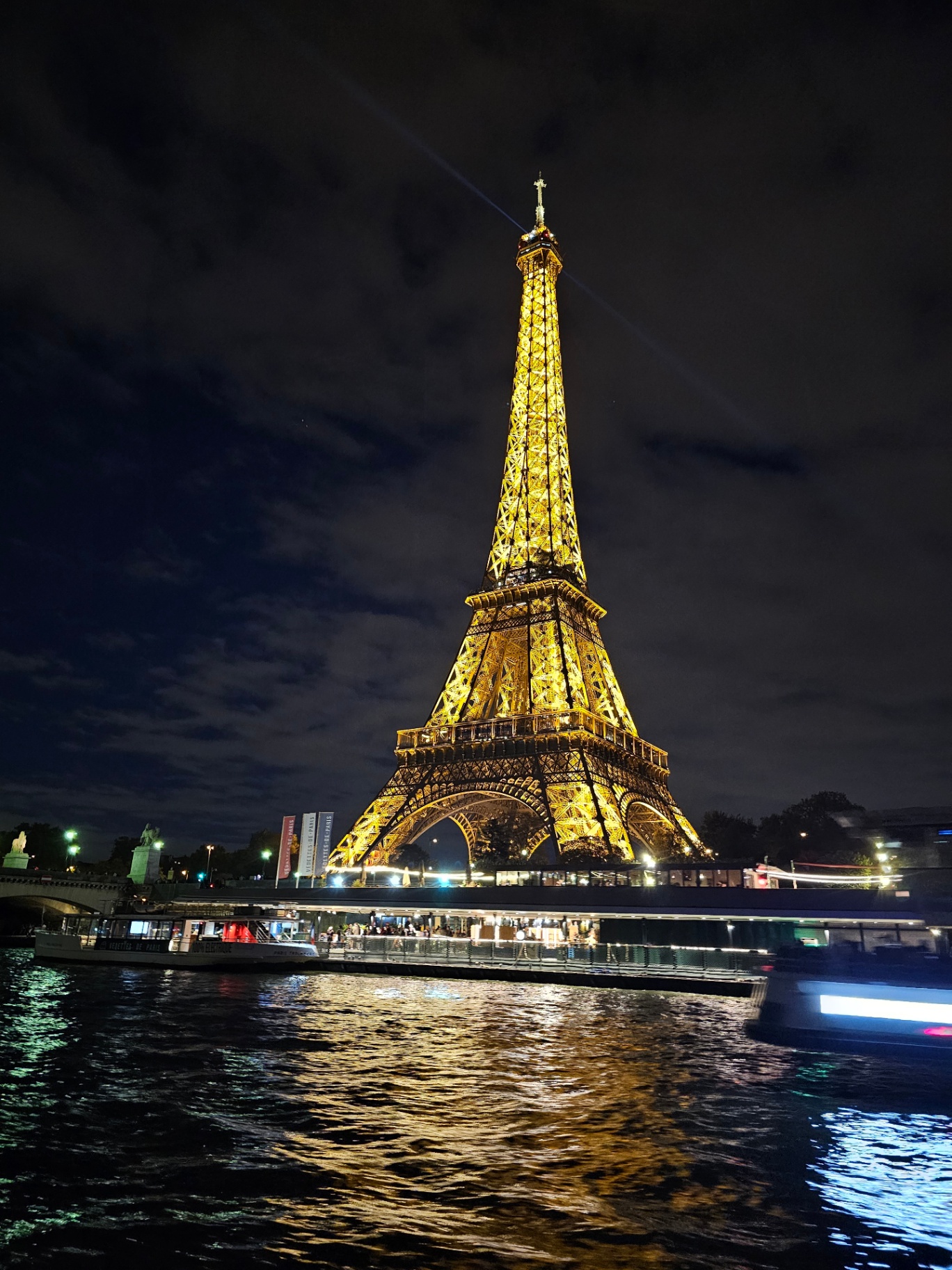 The Eiffel Tower lit gold at night above the Seine